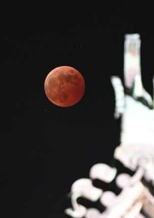 松江城天守の屋根の向こうで、皆既月食により赤銅色に染まった月=8日午後8時8分、松江市殿町