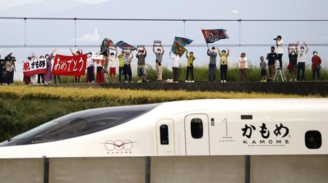 旗や横断幕を手に、西九州新幹線開業を歓迎する人たち＝２３日、長崎県大村市