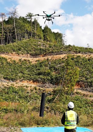 鹿よけ防護柵の支柱をつり下げ、上昇する大型運搬ドローン＝島根県美郷町上野