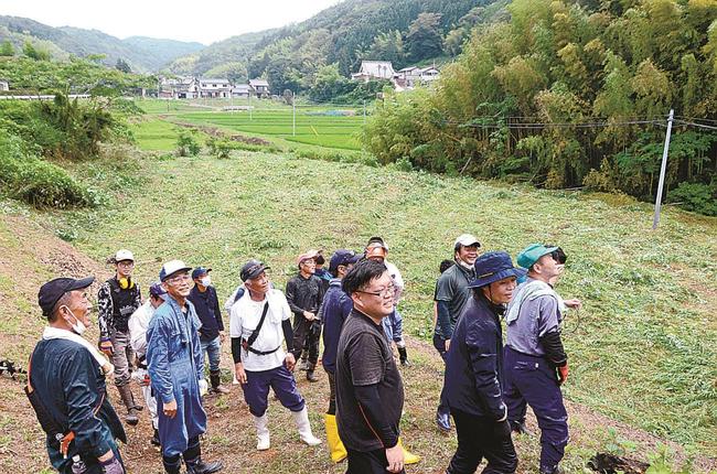 休耕田（中央）の草刈りをほぼ終え、くつろぐ参加者＝出雲市野郷町