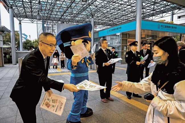 特殊詐欺防止のチラシを通行人に手渡す山陰合同銀行の吉川浩専務執行役員（左）ら∥松江市朝日町、ＪＲ松江駅北口