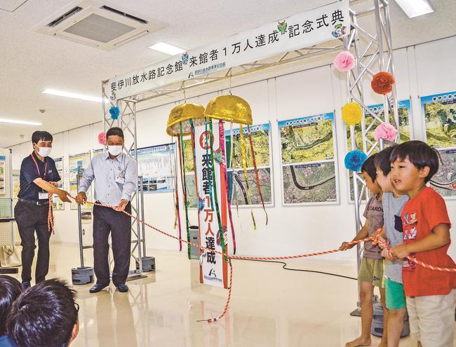 くす玉を割り、１万人達成を祝う関係者＝出雲市上塩冶町、斐伊川放水路事業記念館