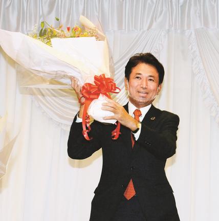 当選確実の報を受け、祝勝会会場で花束を手に喜ぶ飯塚俊之氏＝１１日午後１０時１３分、出雲市塩冶有原町２丁目、ニューウェルシティ出雲
