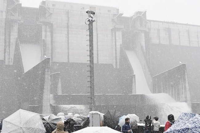 雪の中、非常用水門からの放流を見学する来場者＝雲南市木次町平田