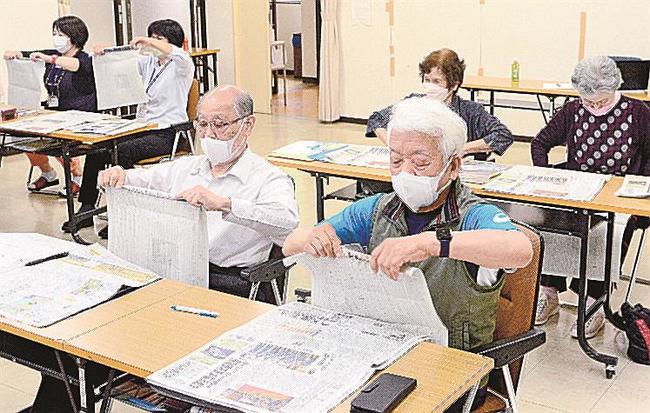 本紙を指先で巻き上げる参加者＝大田市温泉津町小浜、温泉津まちづくりセンター