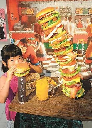 今にも倒れそうな「タワーバーガー」と記念撮影用のバーガーを手にする子ども＝倉吉市鍛冶町１丁目、円形劇場くらよしフィギュアミュージアム
