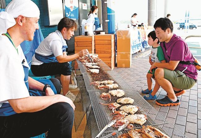 海鮮網焼きの様子を眺める来場者＝浜田市原井町、はまだお魚市場
