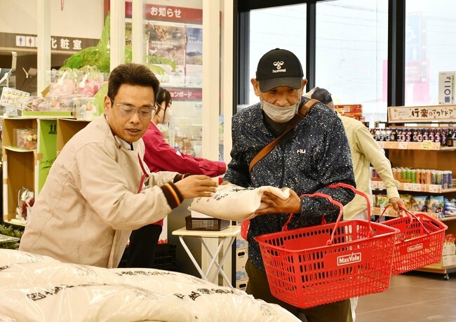 店舗スタッフ（左）から備蓄米を受け取る来店客＝出雲市稲岡町、マックスバリュ川跡店