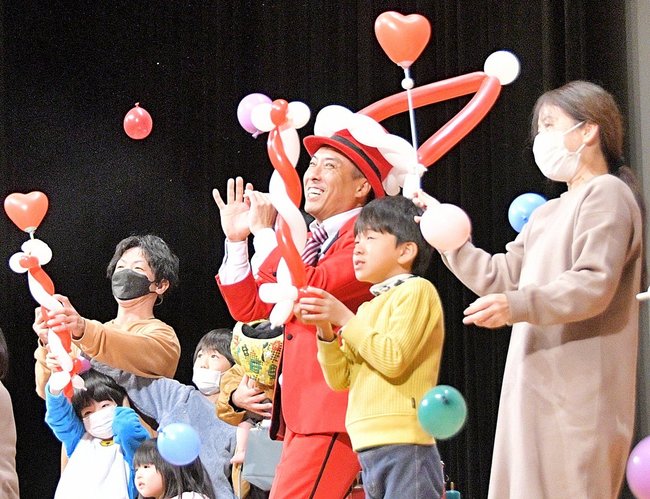 昨年のクリスマスこども大会で、さと原人さん(中央)のバルーンアートを楽しむ親子=2024年12月