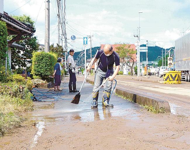 家の前の土砂を流す住民たち＝１３日午前９時１５分、雲南市三刀屋町三刀屋