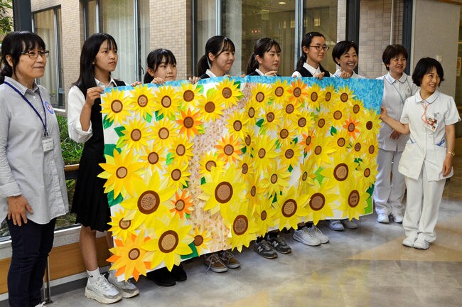 ヒマワリの壁飾りを手に記念撮影する大社高校JRC部の部員と病院関係者=出雲市姫原4丁目、島根県立中央病院