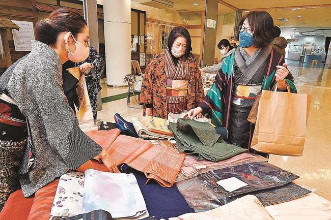 イベントで販売される反物を手に取って確認する、着物を着て訪れた参加者＝松江市白潟本町、スティックビル