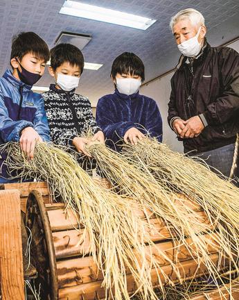 河上清会長（右）に見守られながら、足踏み式脱穀機を体験する児童＝出雲市多伎町口田儀、多伎文化伝習館
