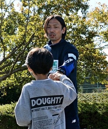 ゴールする参加者をグータッチで迎える鈴木隆行さん＝松江市上乃木丁目、松江総合運動公園