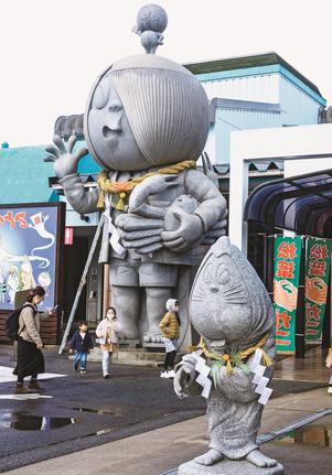 手作りのしめ縄が取りつけられた「がいな鬼太郎」（奥）とねすみ男石像＝境港市竹内団地、大漁市場なかうら