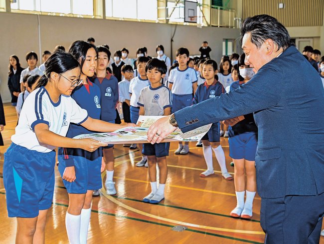 高橋宏聡社長（右）に寄せ書きを手渡す児童代表の川崎結衣さん（左）と三沢葵衣さん＝益田市水分町、吉田南小学校