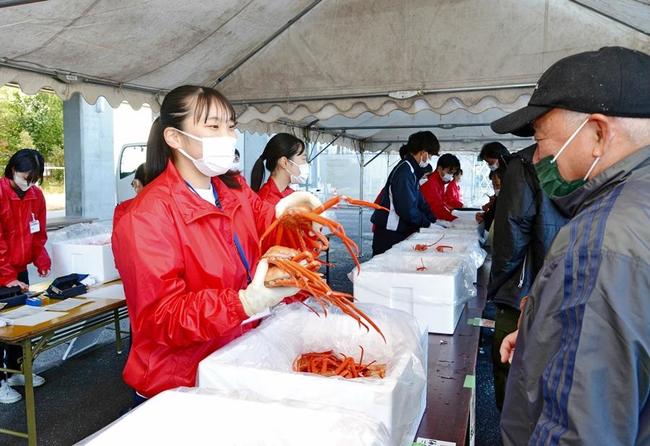 来場者に笑顔でカニを販売する出雲商業高校の生徒＝出雲市大津町