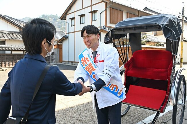 人力車で遊説中にすれ違った有権者と握手する糸賀太郎さん