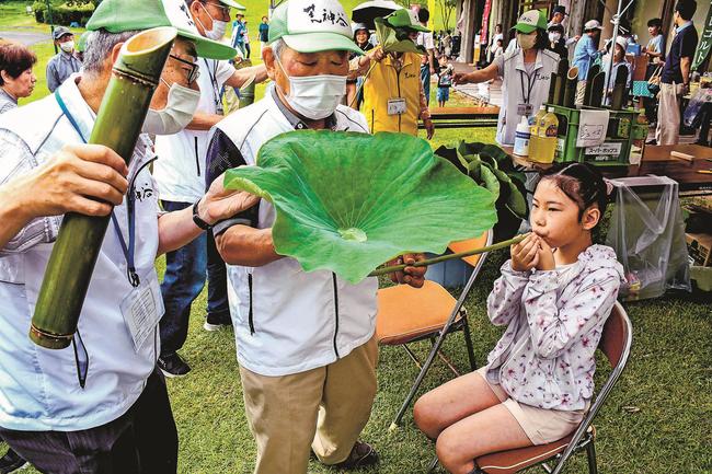 ハスの茎をくわえ、象鼻盃を体験する子ども＝出雲市斐川町神庭、荒神谷史跡公園