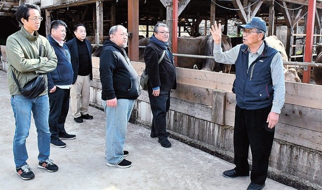 木次乳業の佐藤貞之取締役相談役(右端)から牧場の説明を受ける参加者=雲南市木次町木次、日登牧場