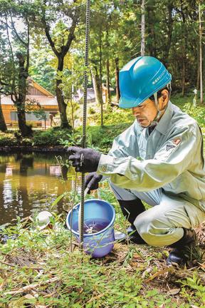 ため池の近くにエノキを植樹し、水やりをするモリアオガエルを守る会会員＝出雲市稗原町、市森神社