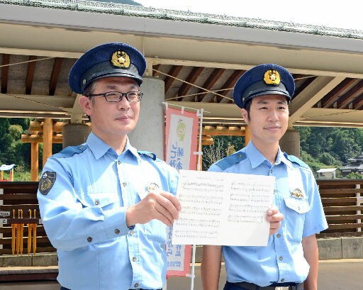 作曲した歌の楽譜を紹介する鎌谷宗和巡査部長（左）と、作詞を担当した松浦裕二巡査部長