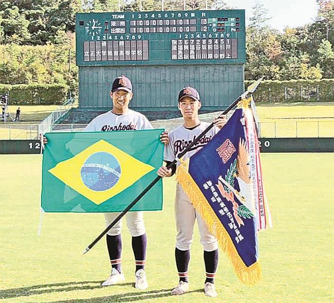 ブラジルの国旗と秋の島根県大会の優勝旗を手にする清水タデウ健次選手（左）と興梠フェリペケンゾウ選手＝松江市上乃木１０丁目、市営野球場（立正大淞南高校提供）