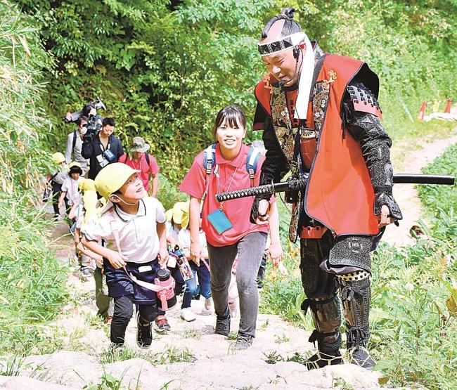 天守台に向かう階段を上る園児と米子城武者隊の山根俊明さん＝米子市久米町、米子城跡