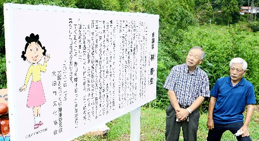 林春生さんの功績を伝える看板を眺める地域住民＝大田市大屋町