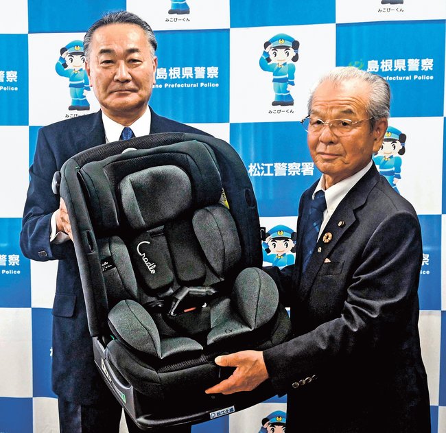 平塚智朗社長（左）からチャイルドシートを受け取る三島進会長＝松江市袖師町、松江署