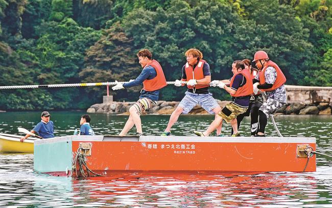 海上の台船の上で、力いっぱい綱を引く参加者＝松江市美保関町北浦、北浦海水浴場