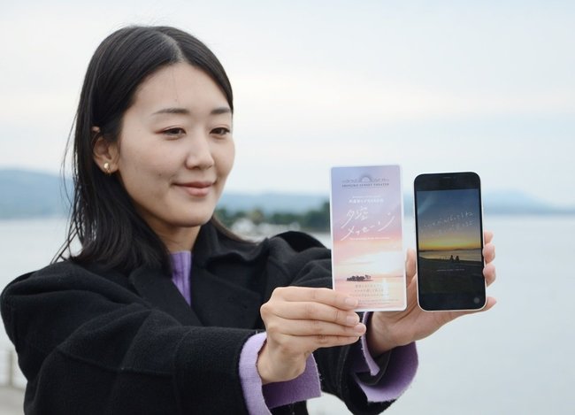 専用のチケット（左）と夕日の景色にメッセージが届いたスマートフォン＝松江市袖師町、岸公園