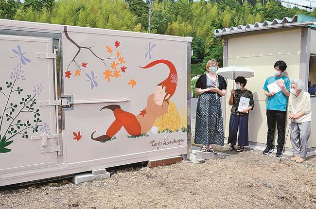米保管庫の壁に描いた絵を説明するタンヤ・セベリカンガスさん（左）＝出雲市多伎町久村、アグリサポートあげ