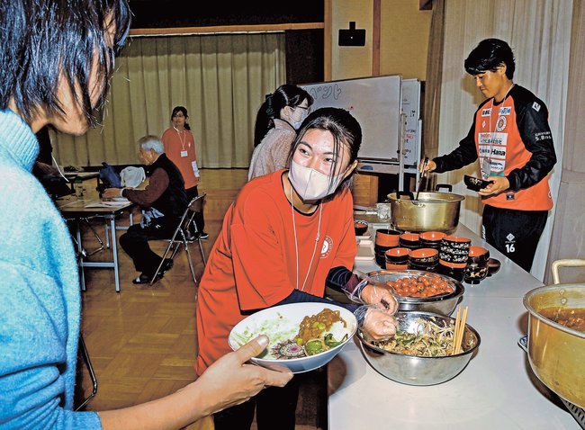 ベルガロッソいわみの曽根嵩之主将（右奥）と給仕をする稲田有咲さん＝益田市遠田町、安田公民館