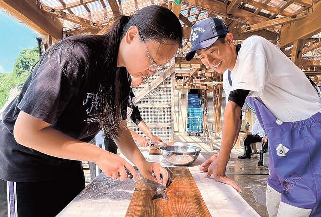 参加者にイサキの三枚おろしを指導する塩見友貴さん（右）＝島根県海士町豊田、海の駅松島