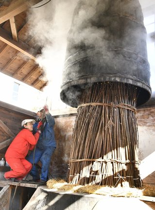 巨大な甑を引き上げ、コウゾの束を取り出す佐々木誠さん、さとみさん夫妻＝江津市桜江町長谷、風の工房