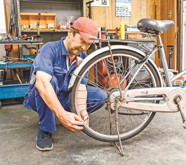 自転車のタイヤの状態を確認する安達憲司整備士＝松江市雑賀町