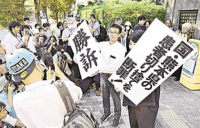 水俣病特別措置法に基づく救済策で対象外となった人たちが国などに損害賠償を求めた訴訟の判決で、「勝訴」などと書かれた紙を掲げる原告側の弁護士ら＝２７日、大阪地裁前