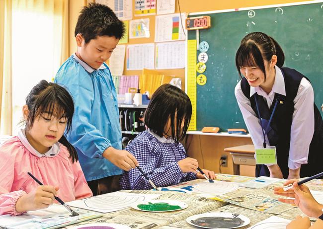 松林瑠那さん（右）からシジミ絵の説明を受け、色塗りする児童＝松江市大輪町、島根大付属義務教育学校