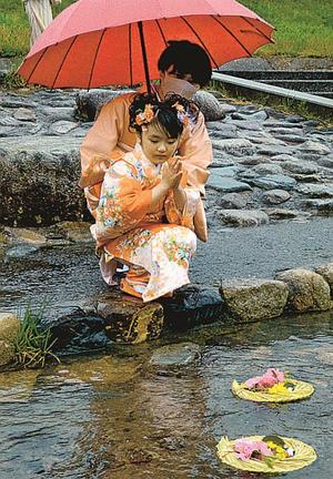 紙製のひな人形を乗せた桟俵を流し、手を合わせる女児＝鳥取市用瀬町用瀬、千代川