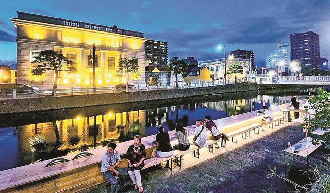 ライトアップされた京橋川沿いのテラスでくつろぐ観光客（２０２３年撮影）