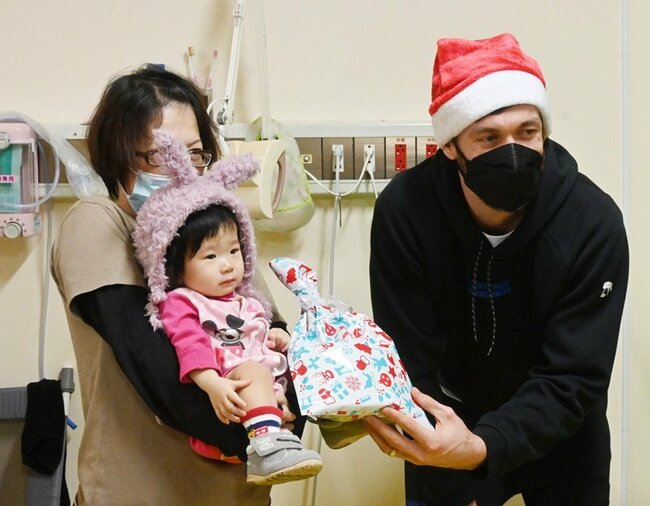 入院している子どもにクリスマスプレゼントを手渡すニック・ケイ選手（右）＝米子市西町、鳥取大医学部付属病院