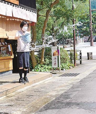 暑さを和らげようと、打ち水をする土産店の従業員＝島根県津和野町後田