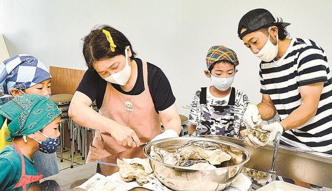 地元のイワガキの殻むきを興味津々で見つめるＩターンした子どもたち＝松江市島根町加賀