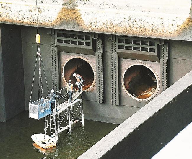 水が抜かれ、姿を現した貯水位維持用の放流設備に入る作業員＝雲南市木次町平田