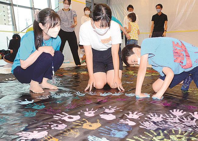 黒い模造紙に手形を付けて花火を描く参加者(右)を見守る山野内聡香さん(中央)=松江市学園南2丁目、松江土建