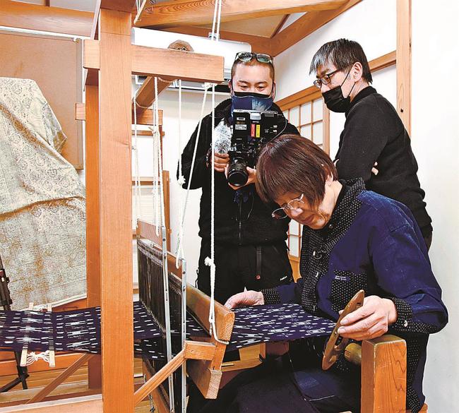 撮影スタッフの前で機織りを実演する永田佳子会長（手前）＝安来市広瀬町広瀬、広瀬絣工房