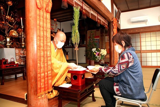 柴田輝住職（左）が昆布ですくった白米を受け取る参加者＝島根県西ノ島町浦郷、常福寺