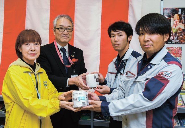 リサイクルトイレットペーパーを贈る平井建設社員（右側）＝安来市中海町、道の駅・あらエッサ