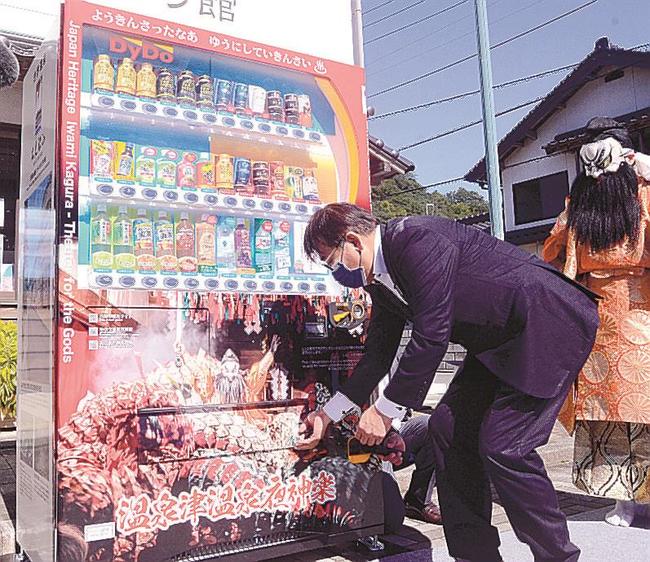 夜神楽をデザインした自動販売機で商品を買う関係者＝大田市温泉津町温泉津、ゆうゆう館前